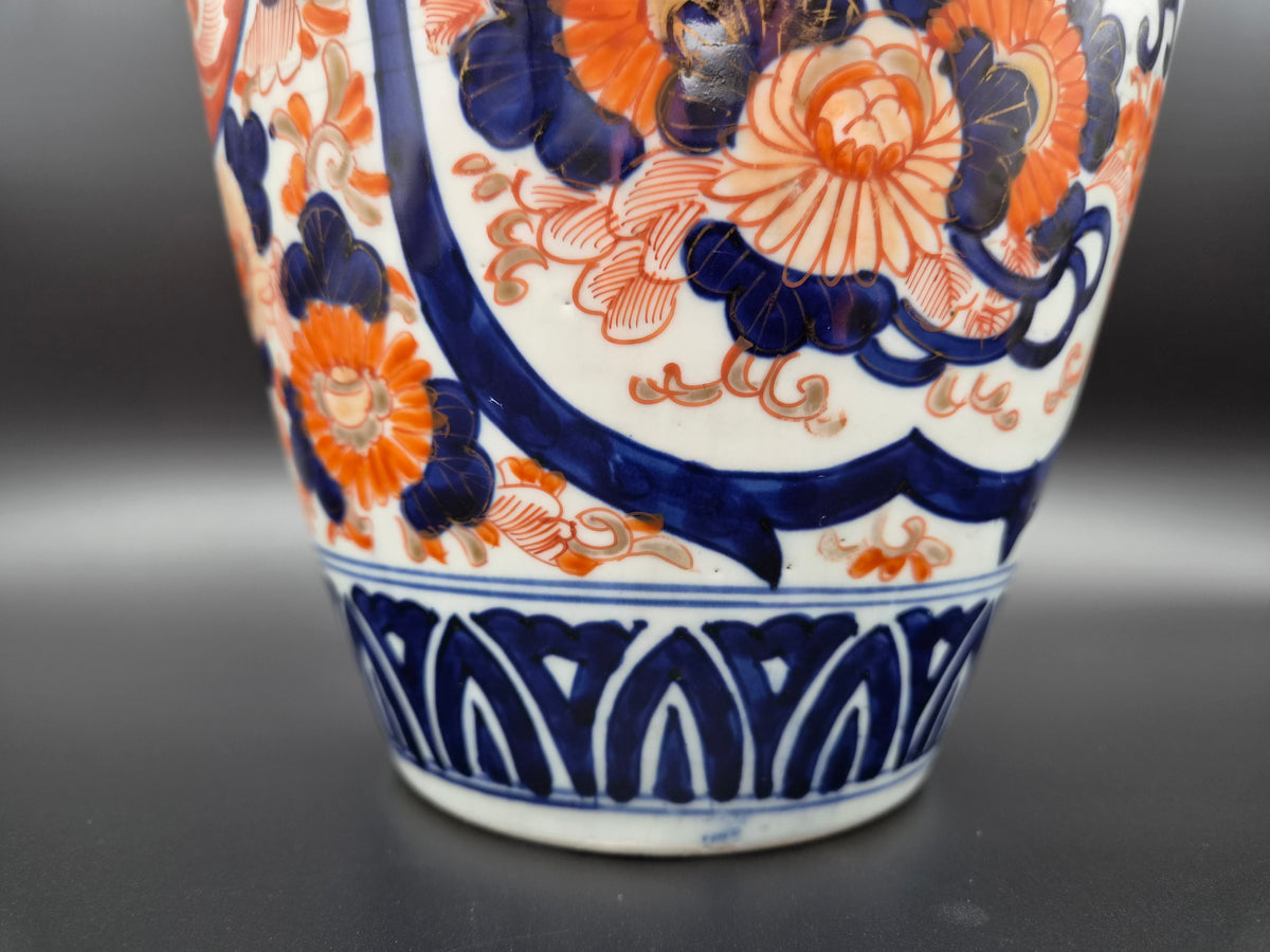 Porseleinen vaas: detail van oranje bloemen en blauwe krullen op witte ondergrond.