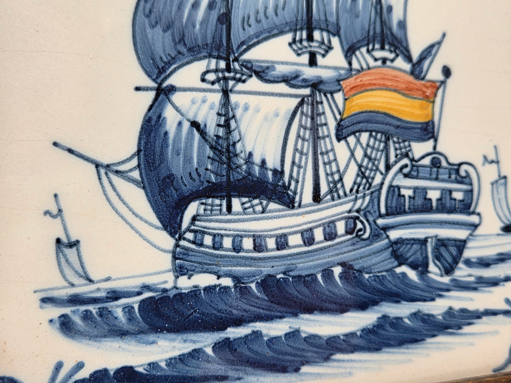 Detail van zeilschip op wandtegel met oranje vlag en donkerblauwe oceaanlijnen