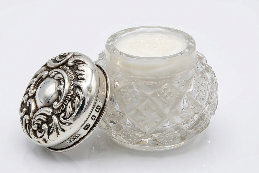 Open potje van geslepen glas met zilveren deksel ernaast