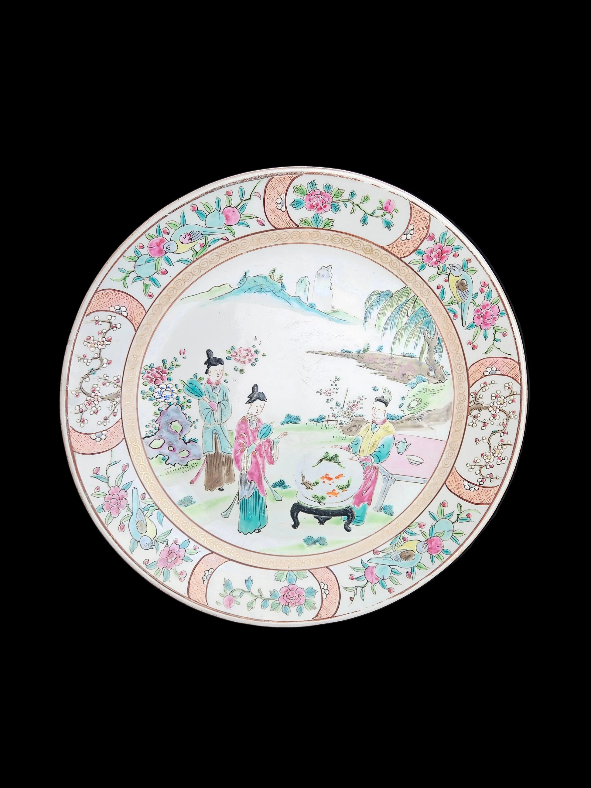 "Antiek Japans Kutani wandbord van 30,5 cm met een handbeschilderde scène van drie figuren in een traditionele Japanse tuin, omringd door een decoratieve rand met bloemmotieven in roze en groen."